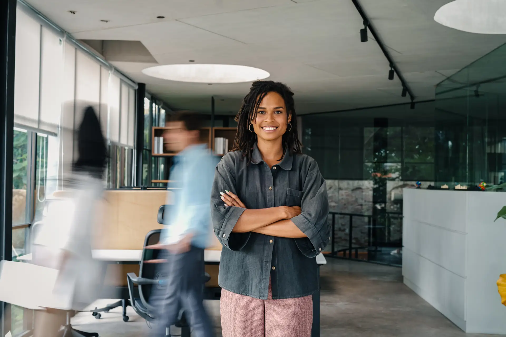 Confident manager standing in a modern office with team in motion behind her