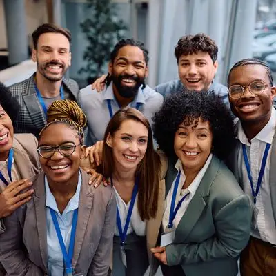 Diverse smiling sales team wearing conference badges in a modern office, illustrating customer relationship management with Slaeb CRM